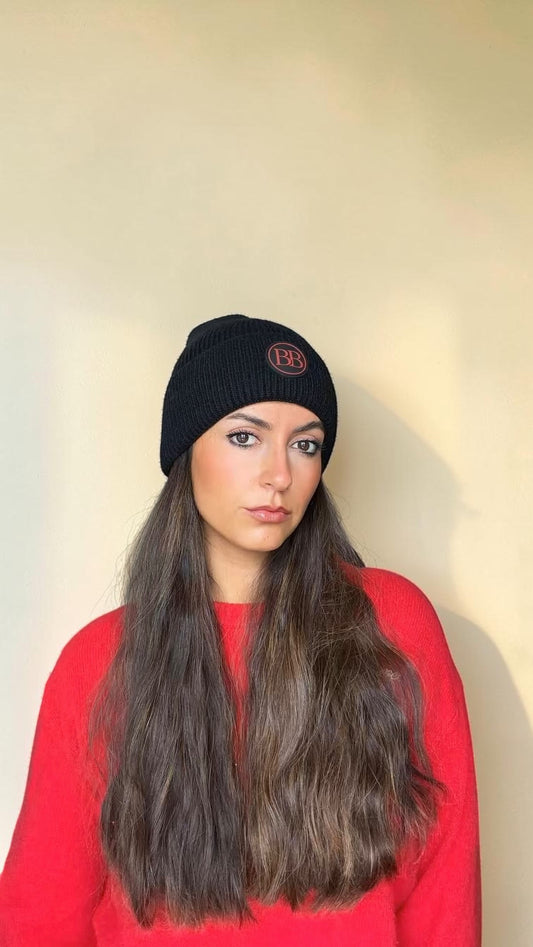 Woman with long hair in a red sweater wearing the black Classic Knit Logo Beanie
