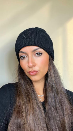 Woman with long hair wearing the black Sherpa Heart Beanie, a ribbed cuffed knit with a black heart patch