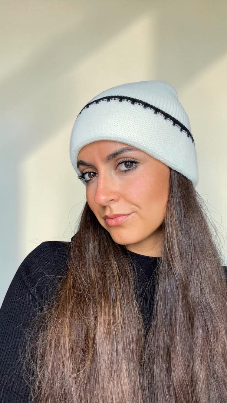 Close-up of the ivory knit beanie with black contrast stitching along the cuff, worn over long hair