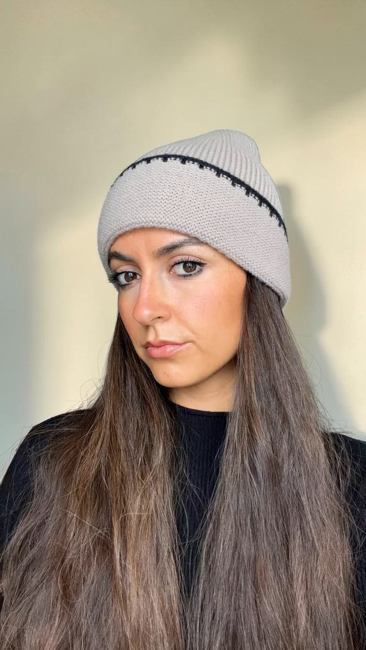 Close-up of the taupe knit beanie with black contrast stitching along the cuff, worn over long hair